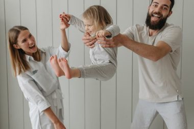 Joyful parents playing with their daughter indoors, all wearing white, capturing a moment of happiness.